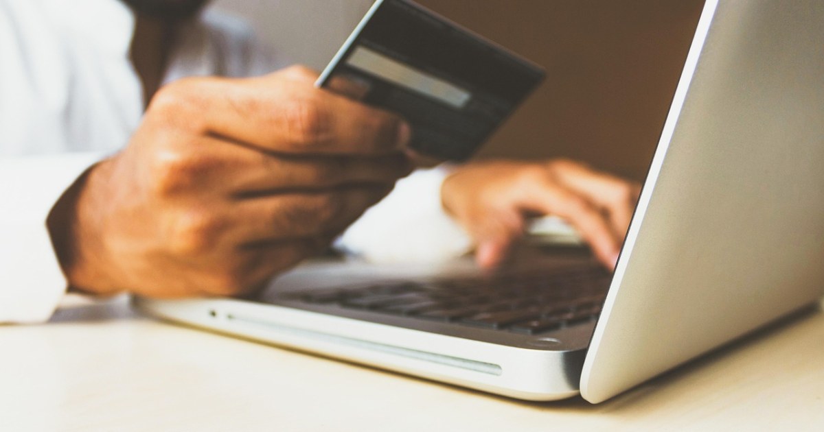 Person holding a payment card while using a laptop for an online SaaS billing cost comparison.