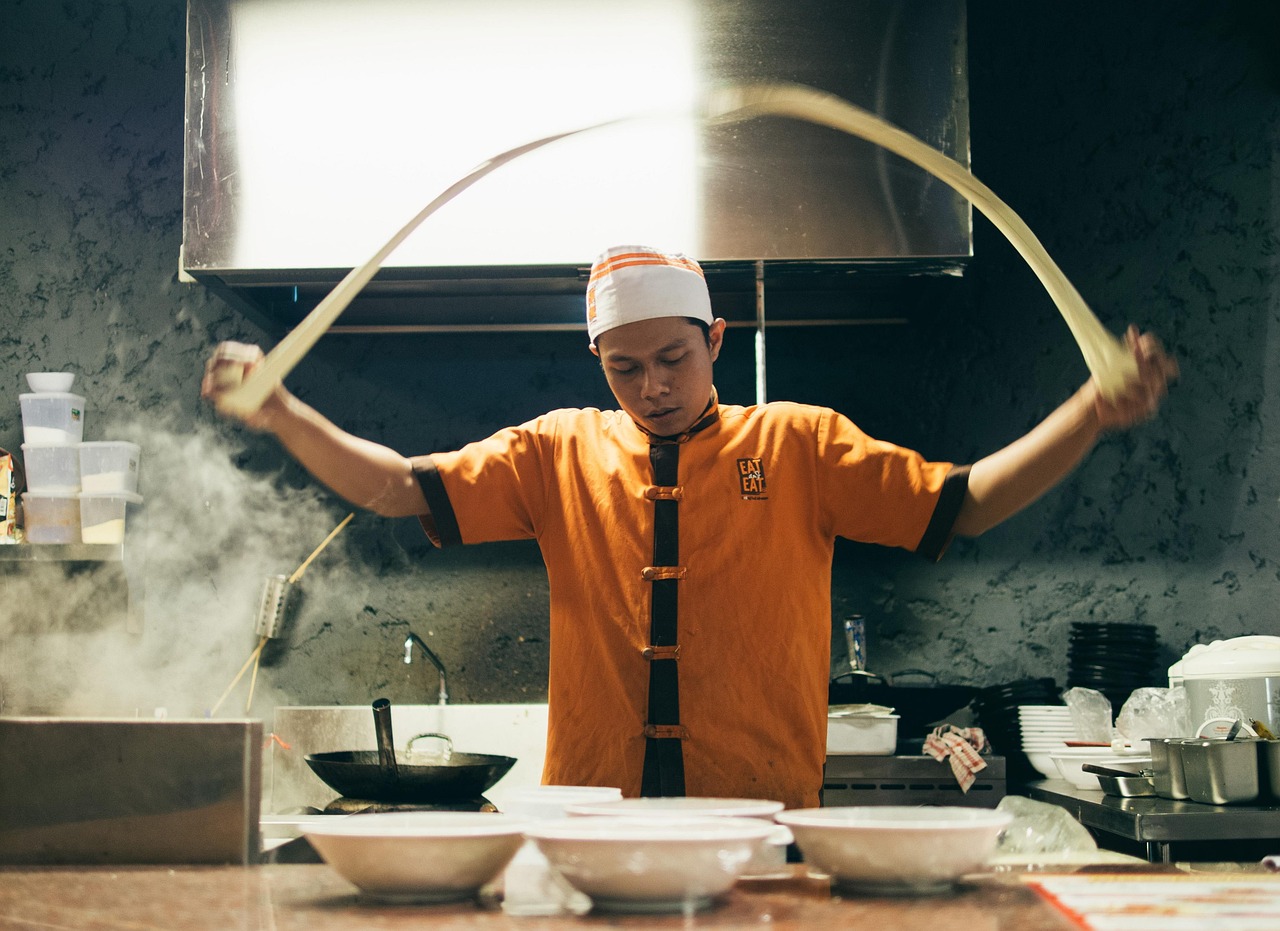 A chef stretching fresh noodles in an Asian restaurant kitchen; illustrative image, not a still from Awkwafina: The Unlikely Cook.