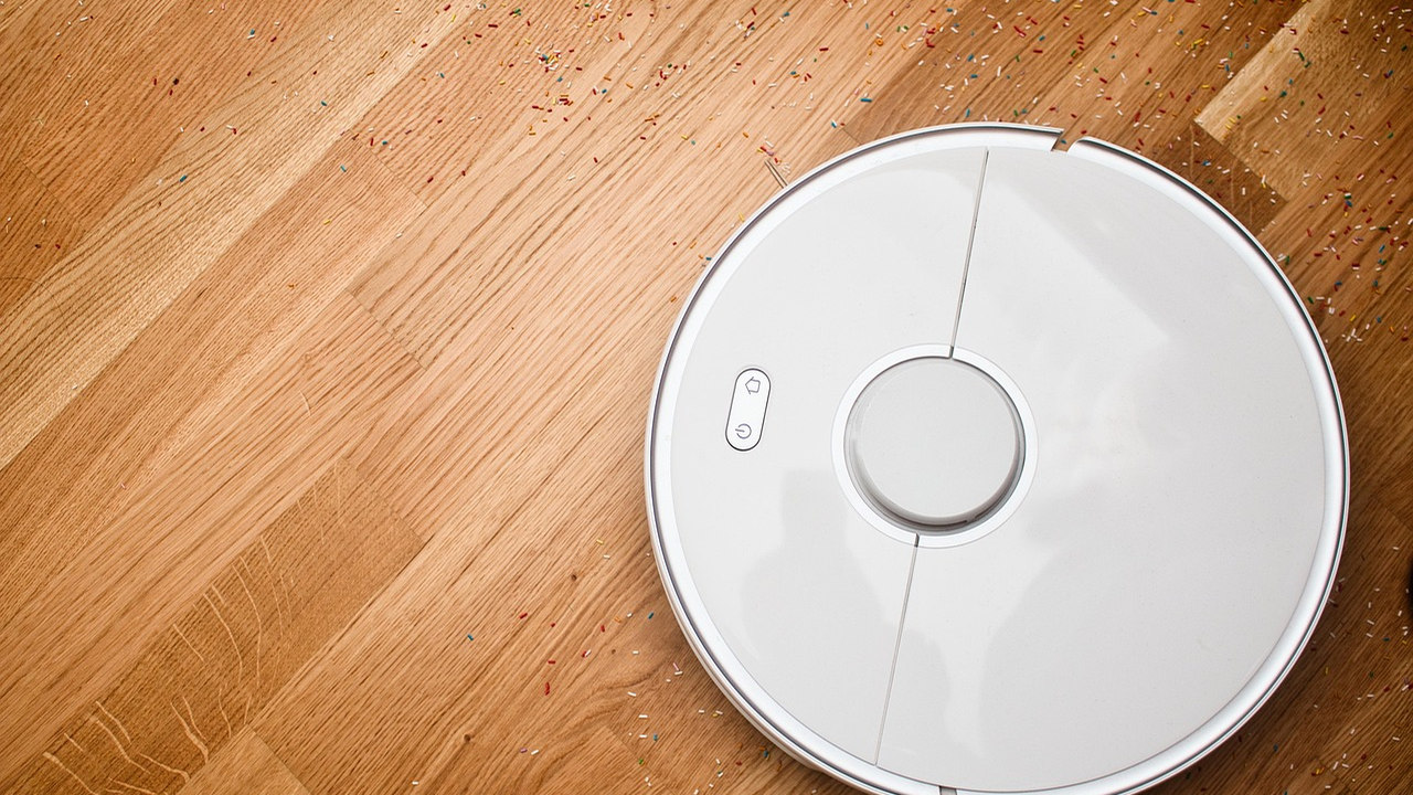 White circular robotic vacuum cleaner seen from above on a wooden floor
